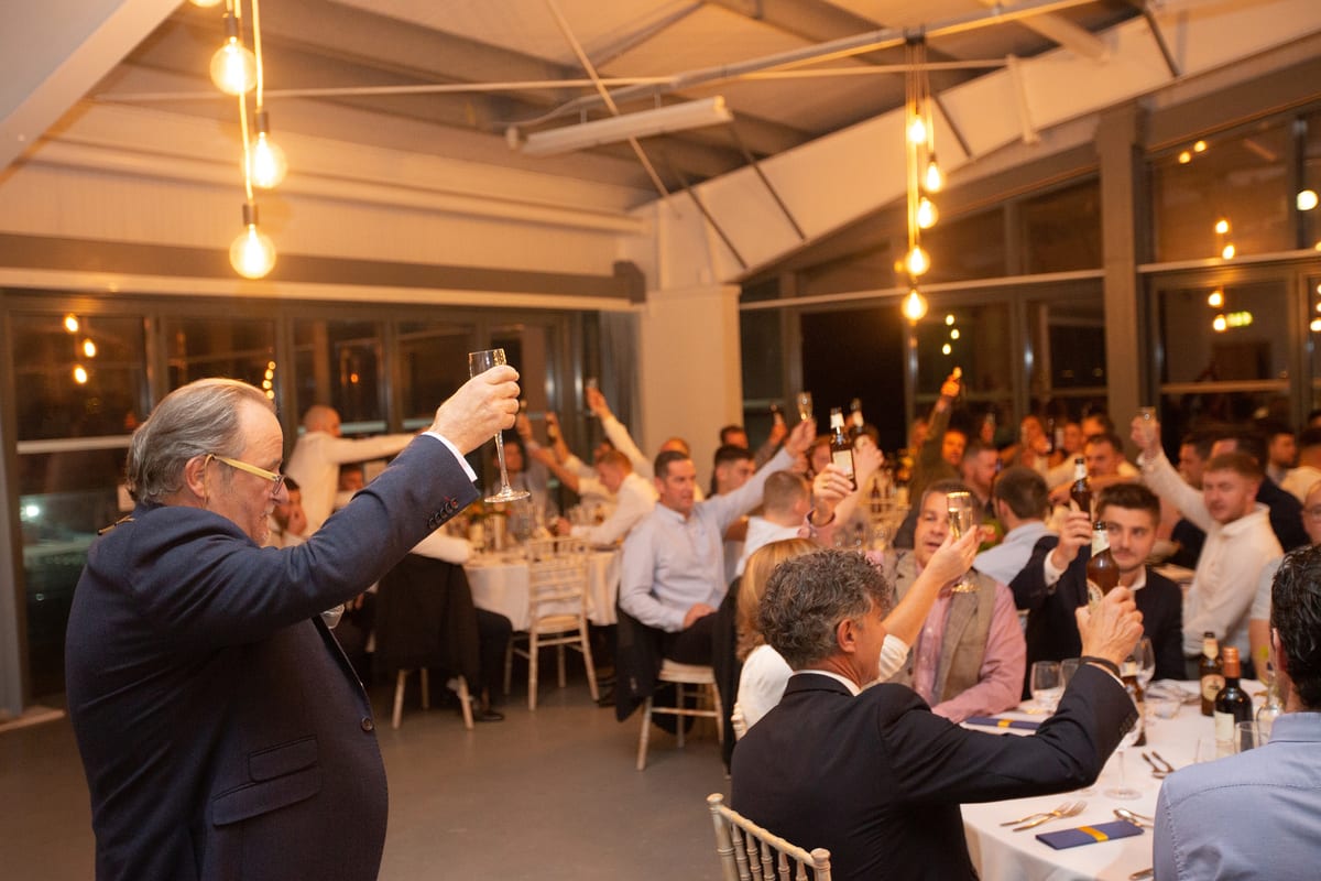 Guests raise glasses in a celebratory toast during Pendennis’ 2021 apprentice graduation dinner, under warm ambient lighting.