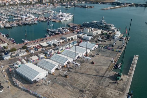 Aerial view of the America's Cup team village and foiling yachts at Pendennis Vilanova during regatta setup.