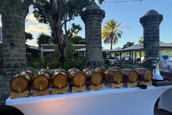 A row of small personalised rum barrels and silver trophies displayed on a white tablecloth in the gardens of The Admiral’s Inn, ready for the Antigua Superyacht Challenge prizegiving.