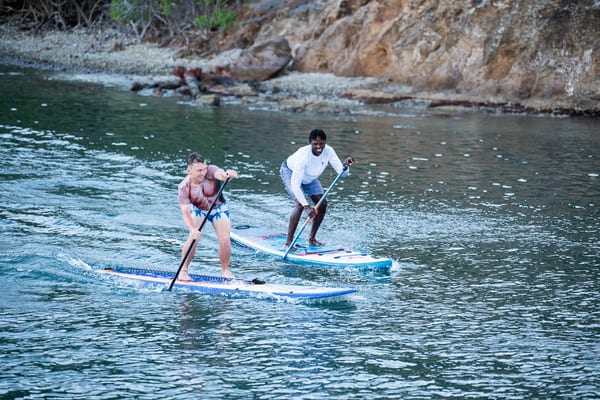 Two competitors racing side by side on paddleboards during the Antigua Superyacht Challenge charity event, with determined expressions and water splashing around them.