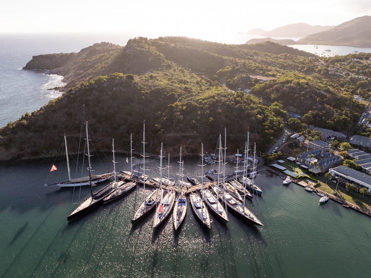 Aerial view of superyachts lined up at the dock in Nelson’s Dockyard, Antigua, surrounded by lush hills and calm evening light during the Antigua Superyacht Challenge.