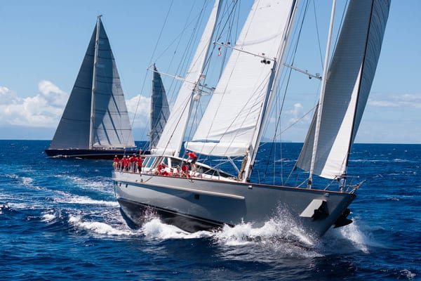 Superyacht Catalina powers through the waves during the 2025 Antigua Superyacht Challenge, her crew in red shirts focused on performance as other yachts race behind in the blue Caribbean sea.