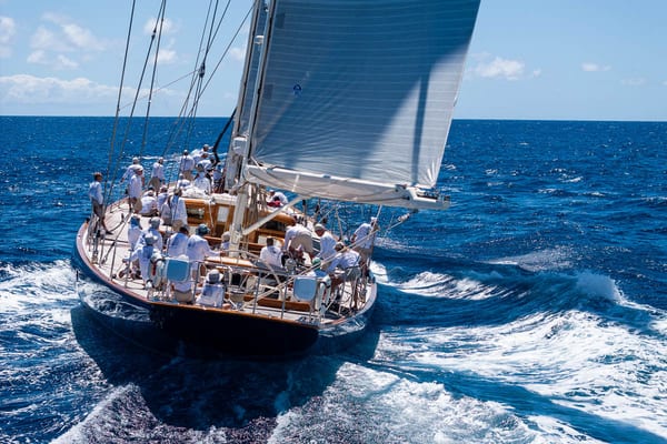 Superyacht Rebecca sails downwind during the 2025 Antigua Superyacht Challenge, with her full crew dressed in white team shirts and focused on performance under the Caribbean sun.