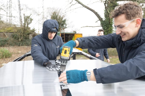 Pendennis apprentices fixing a roof panel into place with a drill during a Community Week shelter project.