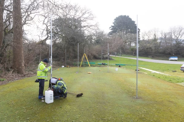 Pendennis apprentices installing metal posts on a grassy outdoor area using spirit levels and measuring tools.