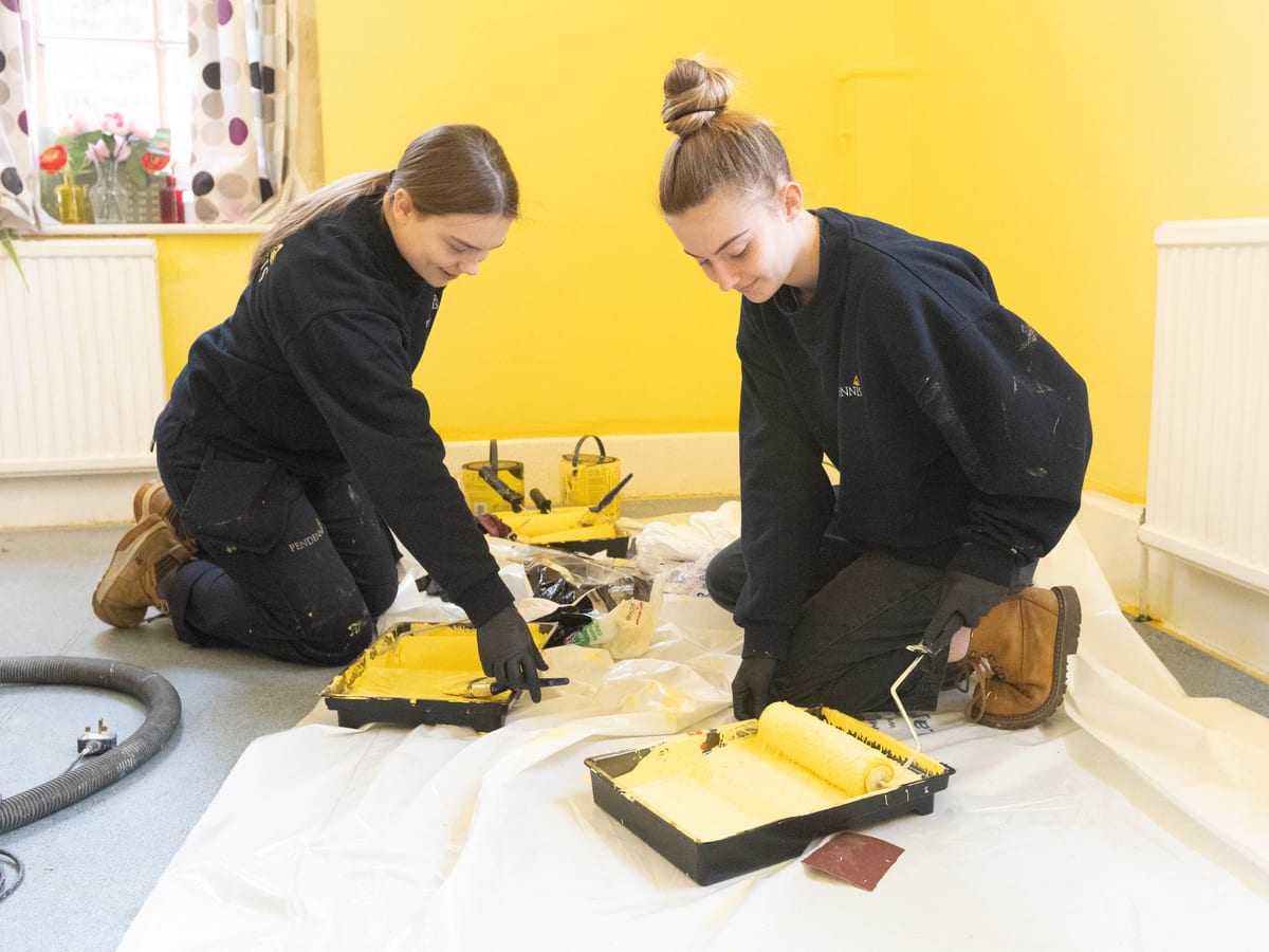 Two Pendennis apprentices kneeling on a dust sheet and preparing paint rollers during Community Week.