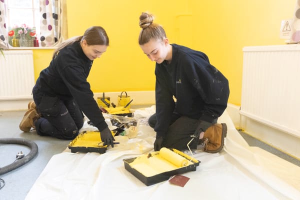 Two Pendennis apprentices kneeling on a dust sheet and preparing paint rollers during Community Week.