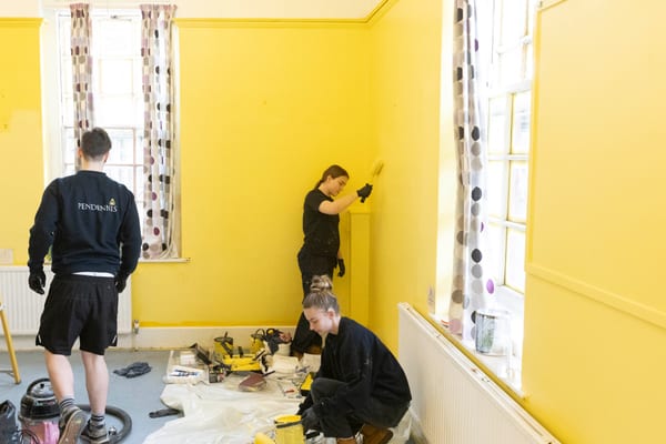 Pendennis apprentices painting and decorating a bright yellow community room during Community Week 2025.