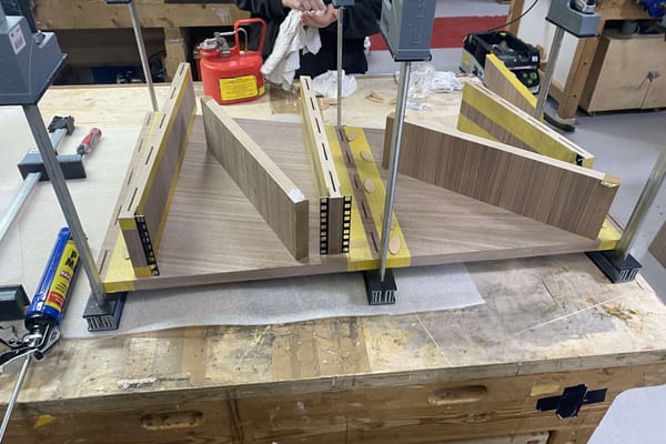 Wooden cabinet parts held in clamps during assembly on a workbench in the Pendennis joinery workshop.