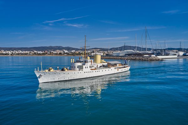 Classic motor yacht Marala cruising near the marina at Pendennis Vilanova under clear blue skies.