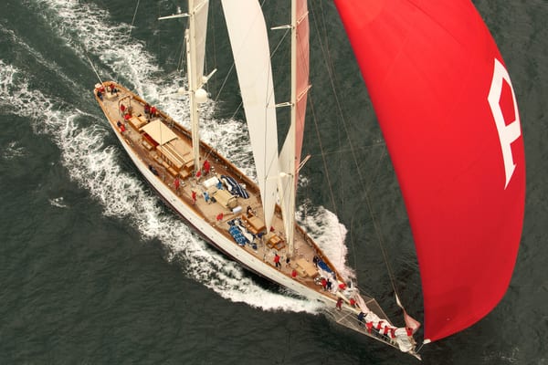 Aerial view of Adela racing with full sails during the 2010 Pendennis Cup, featuring a striking red spinnaker with a white "A".