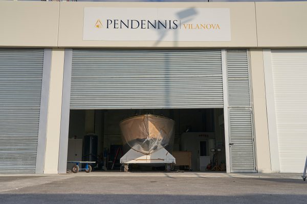 A yacht hull inside Pendennis Vilanova’s newly completed paint facility, viewed through a partially open industrial door.