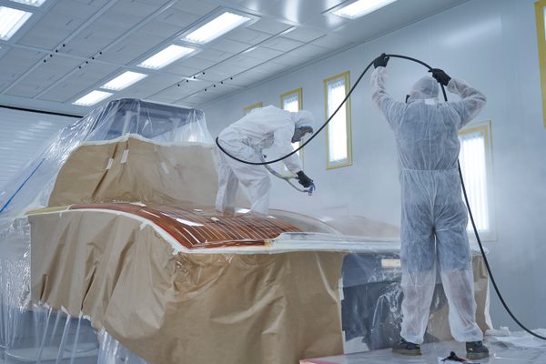 Technicians in protective suits spray painting a yacht inside Pendennis’s advanced paint facility.