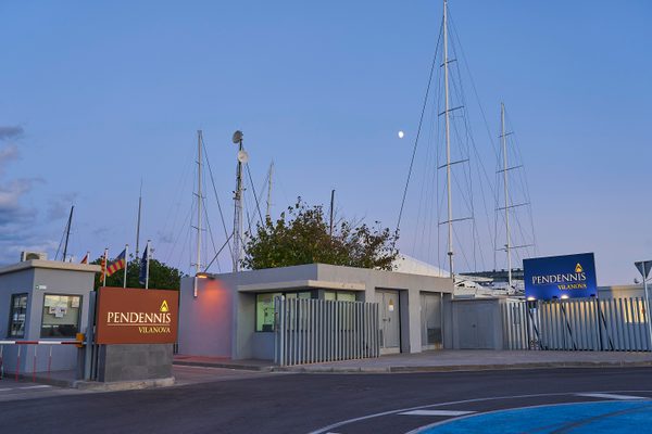 Entrance to Pendennis Vilanova at dusk with new illuminated signage and yacht masts visible behind the gates.