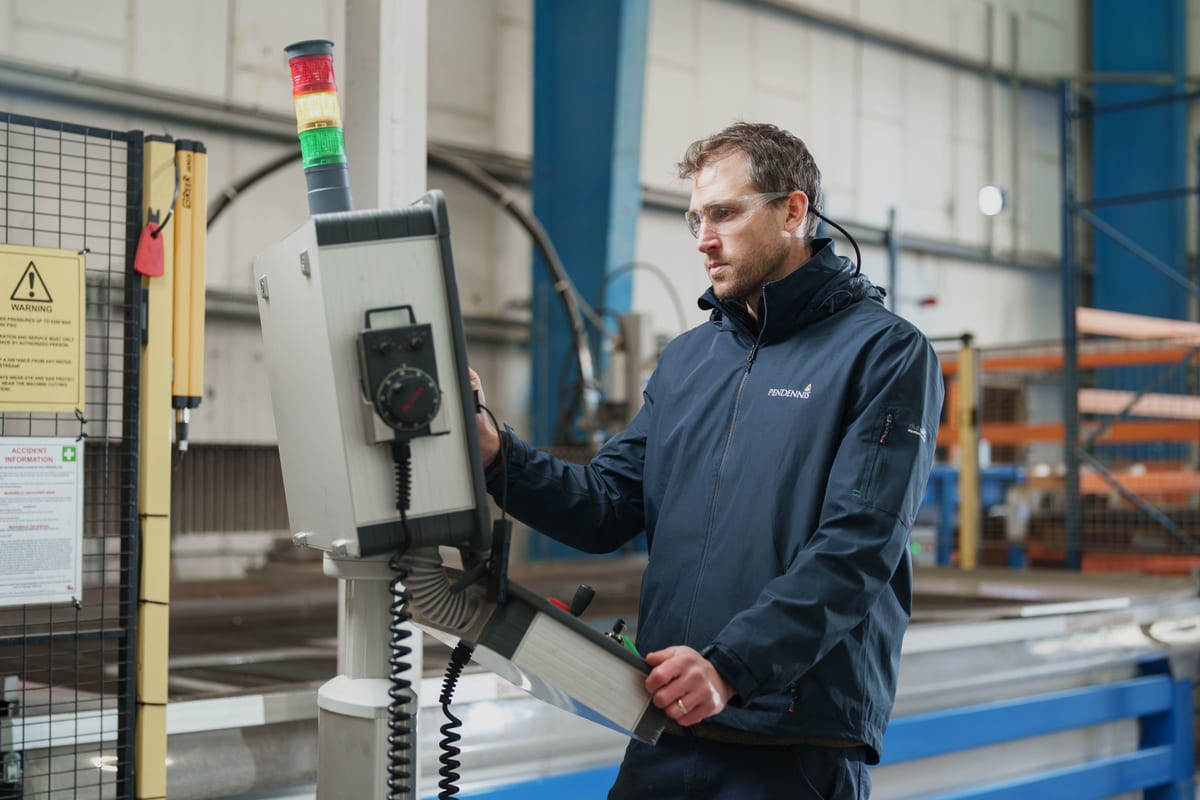 Technician using control panel at Pendennis’s Digital Manufacturing Centre, wearing safety glasses and branded jacket.