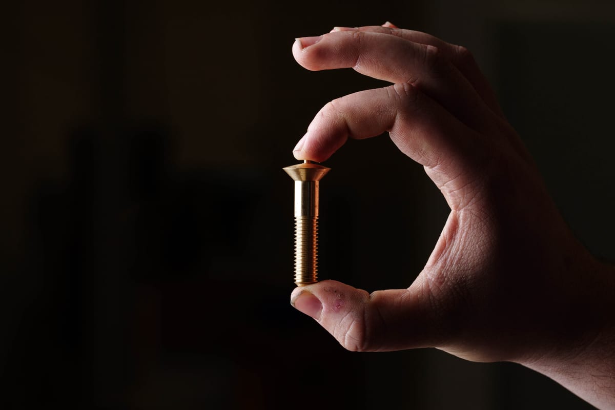 Hand holding a precision-machined brass component, highlighting fine detail and craftsmanship at Pendennis.
