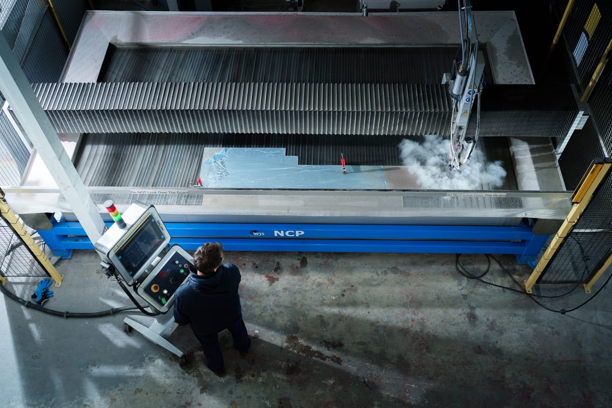 Overhead view of a Pendennis team member operating a waterjet cutter on a large metal sheet at the digital manufacturing centre.