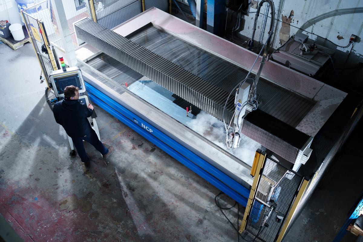 Engineer using control panel to operate waterjet cutting machine on a large metal sheet at Pendennis's digital facility.
