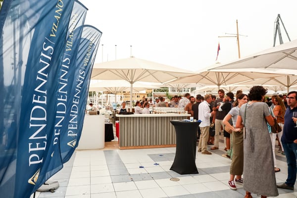 Guests gather under umbrellas at Pendennis Vilanova’s Superyacht Cup Palma event, with branded flags in the foreground.