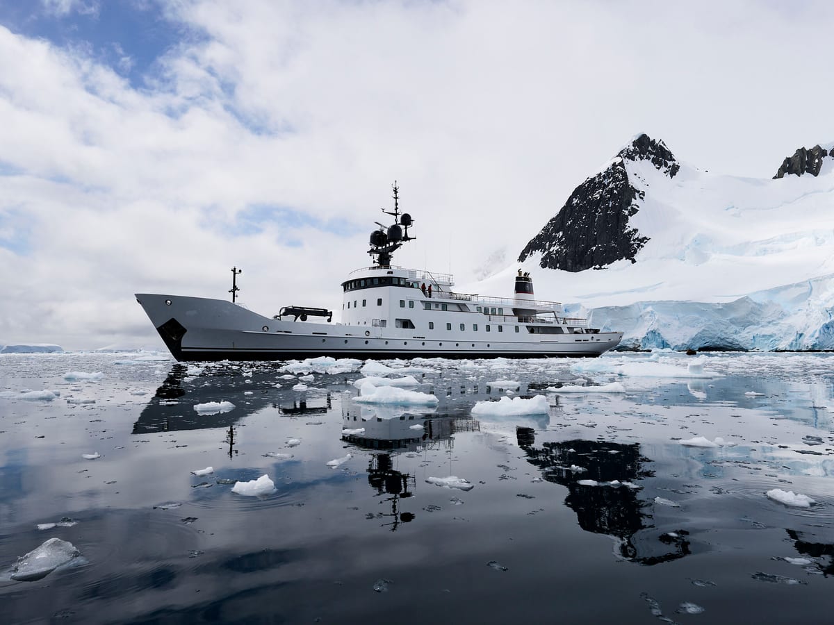 Explorer yacht Jester navigating icy waters in Antarctica with snow-covered mountains in the background.