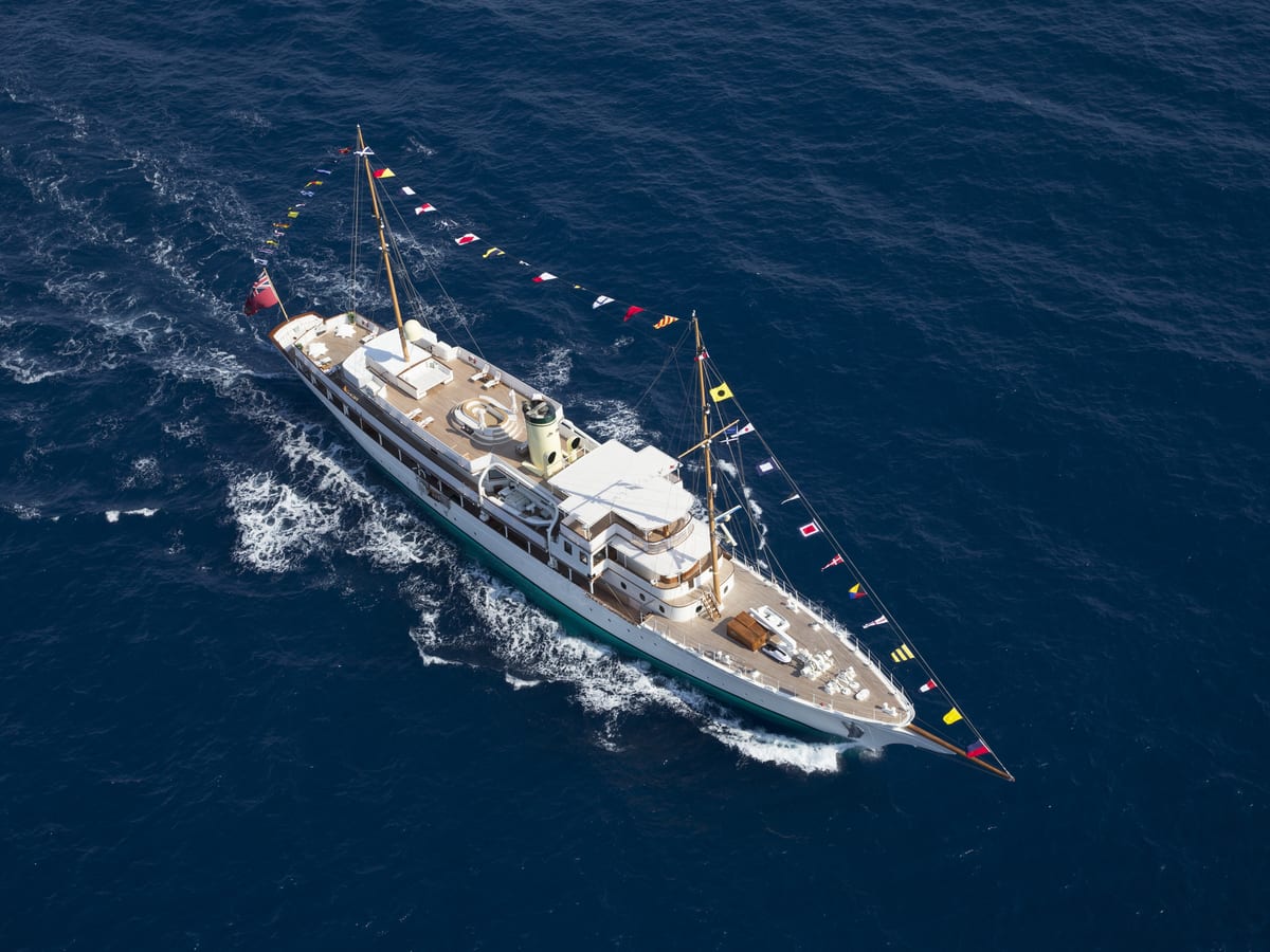 Aerial view of classic motor yacht Haida 1929 cruising at sea, adorned with colourful maritime signal flags along its rigging.
