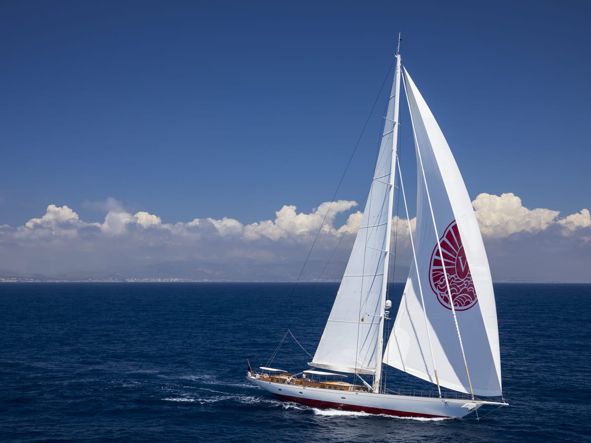 Sailing yacht Vijonara glides through deep blue waters under full sail, with her distinctive red emblem visible on the foresail.