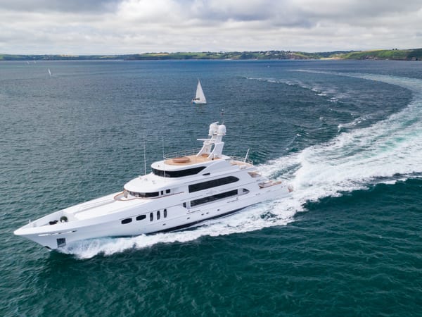 Superyacht White Star cruises at speed after refit, leaving a sweeping wake across the water near the Cornish coast.