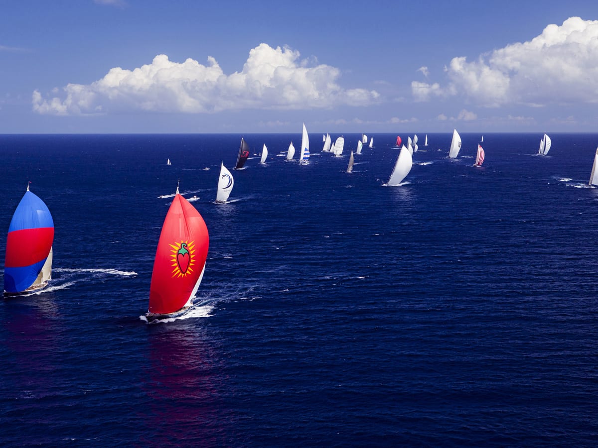 Dozens of superyachts with colourful spinnakers race across deep blue waters under a bright sky at the St Barths Bucket Regatta.