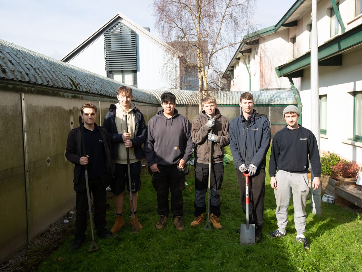 Group of Pendennis apprentices standing with tools in a grassy courtyard, preparing for outdoor maintenance work.