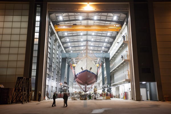 Classic three-masted schooner Adix in the Pendennis Falmouth build hall, suspended by travel hoist during nighttime operations.