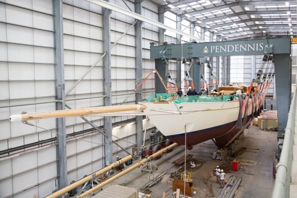 Adix suspended inside the Pendennis build shed as refit work continues, with her masts and rigging laid out nearby.