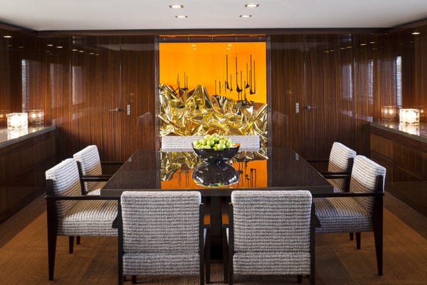 The formal dining room aboard motor yacht A2, featuring a glossy dark table, textured armchairs, and a striking contemporary gold and orange wall sculpture.