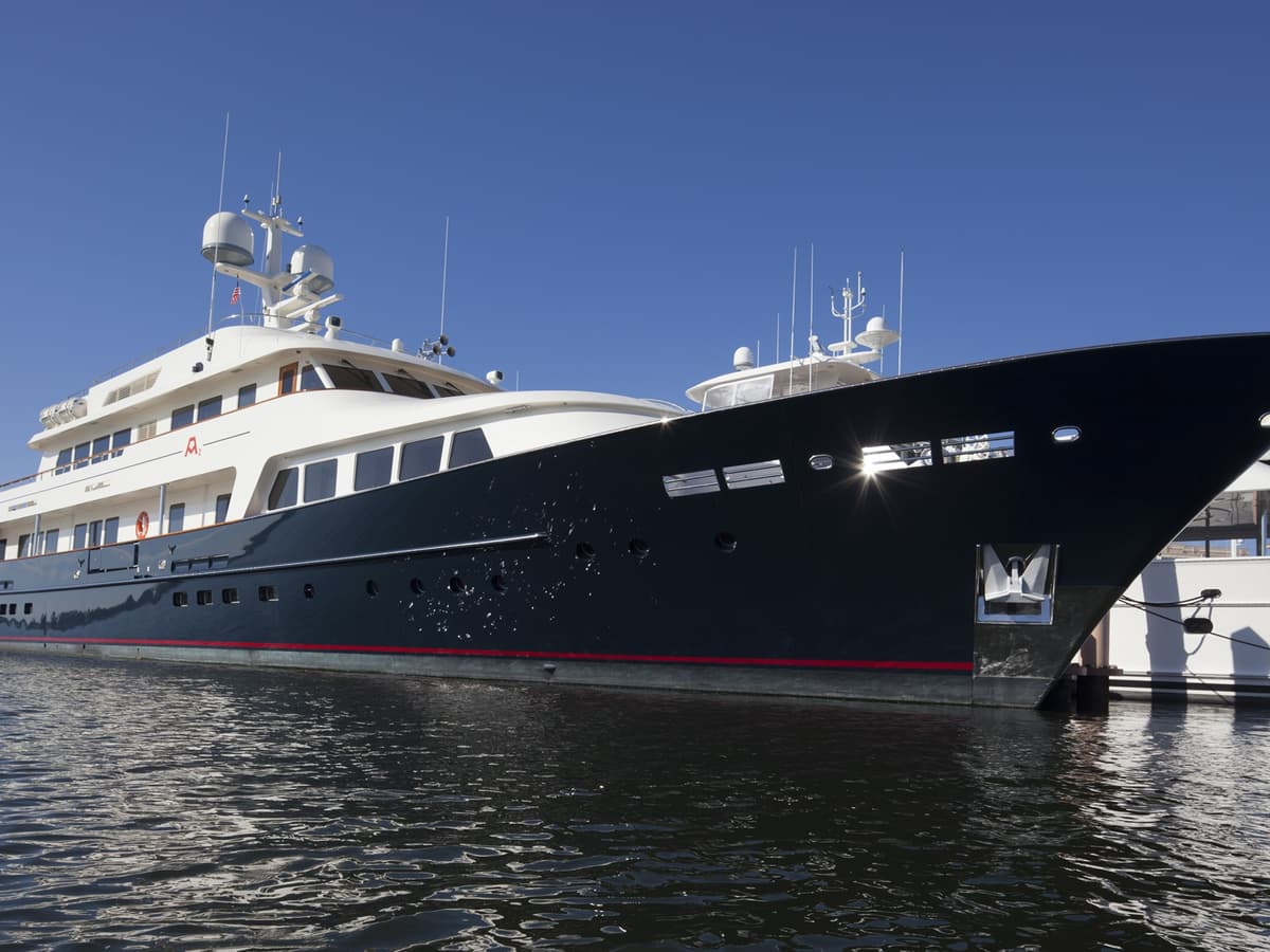 Low-angle view of the motor yacht A2 docked in calm water, its deep navy-blue hull reflecting the light, with a bright white superstructure and radar domes under a clear blue sky.