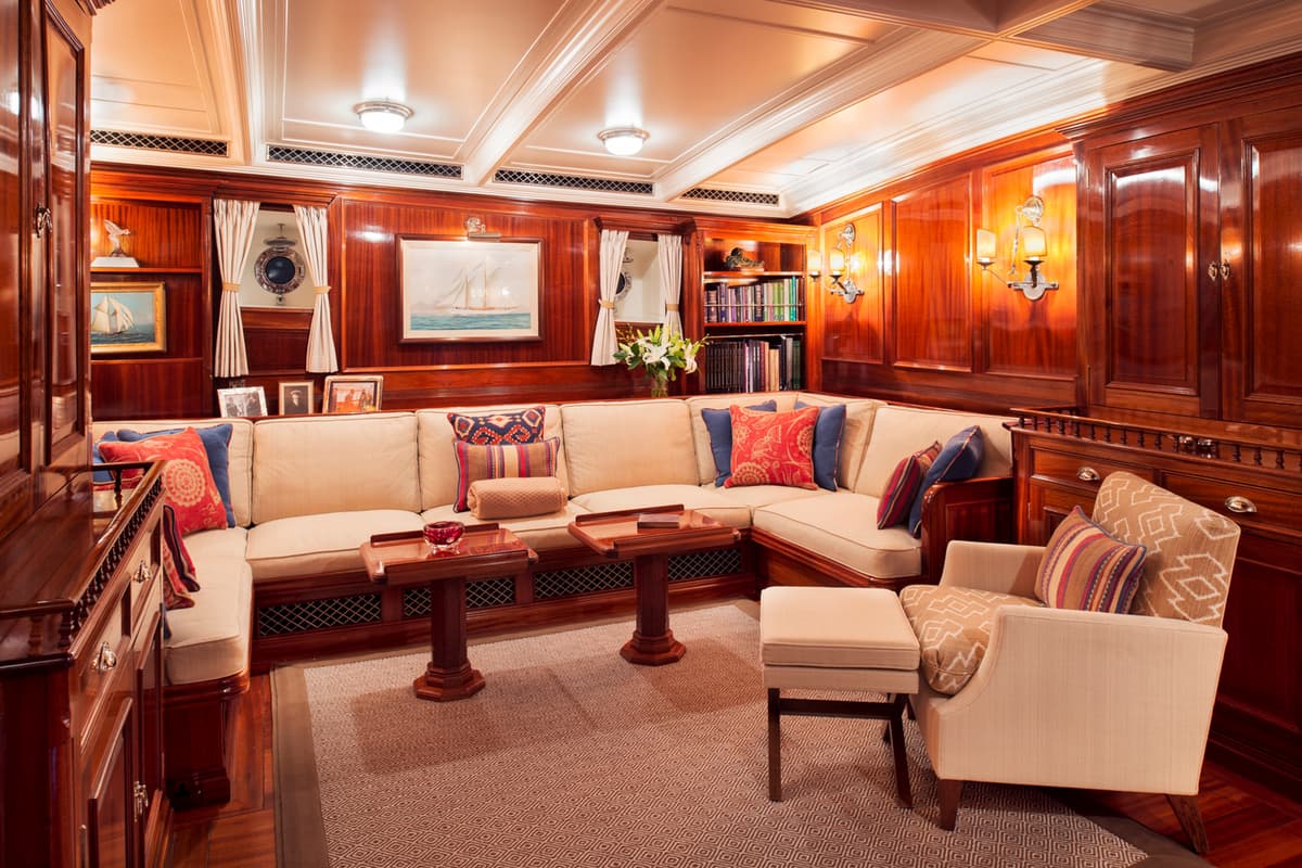 The main salon of Adela, featuring rich wood paneling and cream upholstery, refurbished by Pendennis' Interior Design team during the 2012 refit.
