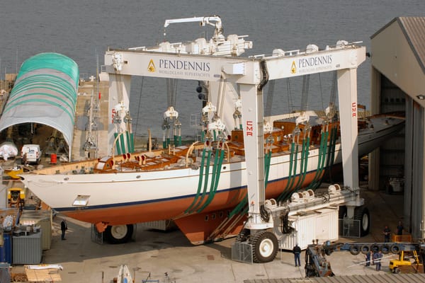 Classic three-masted schooner Adix being transported by a 400-ton mobile hoist into Pendennis’ main shed during her 2009 refit, with green lifting straps supporting the hull.