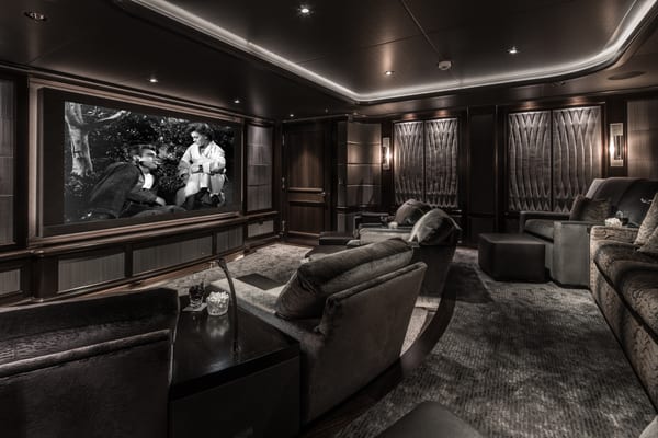 Aquila superyacht’s private cinema with luxurious reclining armchairs, dark panelled walls, plush carpeting, and a large screen showing a classic black and white film.