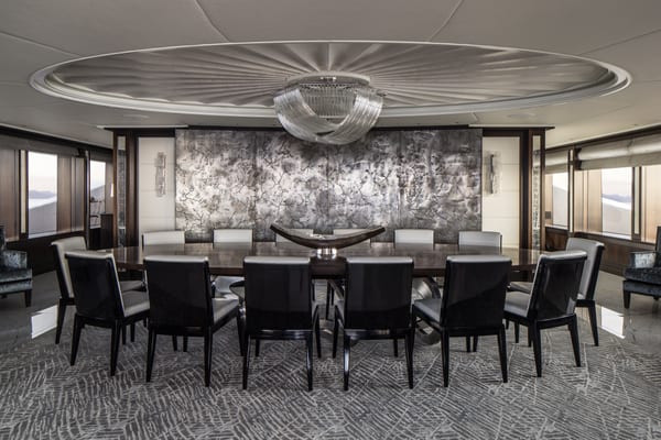 Aquila superyacht's main dining room featuring a large formal dining table, contemporary black and white chairs, a textured feature wall, and a statement chandelier.