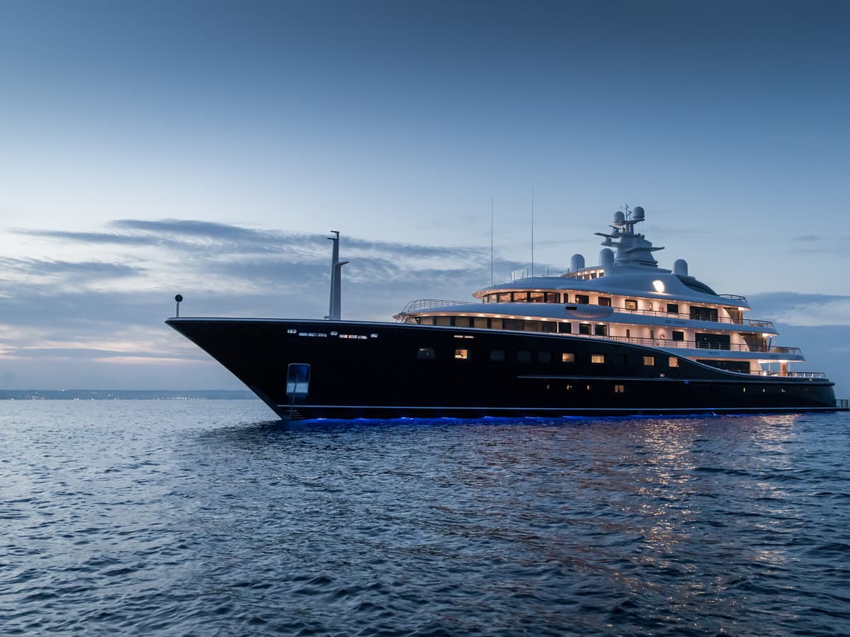 Superyacht Aquila illuminated at dusk, cruising on calm waters.