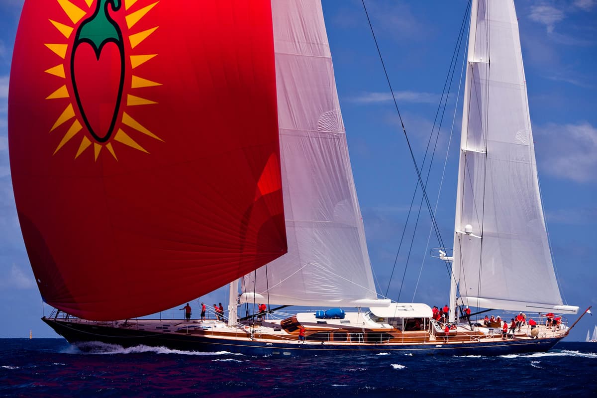 Christopher racing at the 2011 St Barths Bucket, with a red spinnaker sail featuring a chili pepper design, sailing on the clear blue waters with crew visible on deck.
