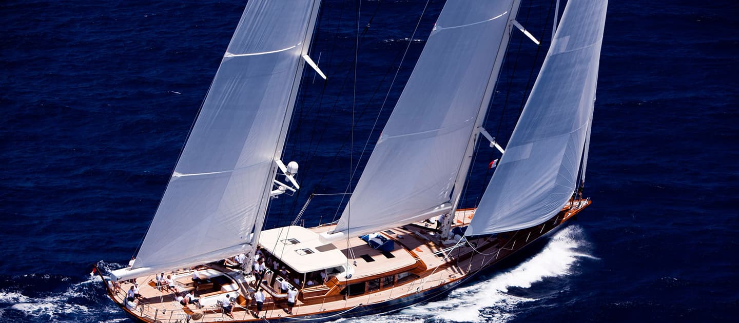 Christopher sailing with full sails up in the deep blue sea, with a crew visible on deck during a race.