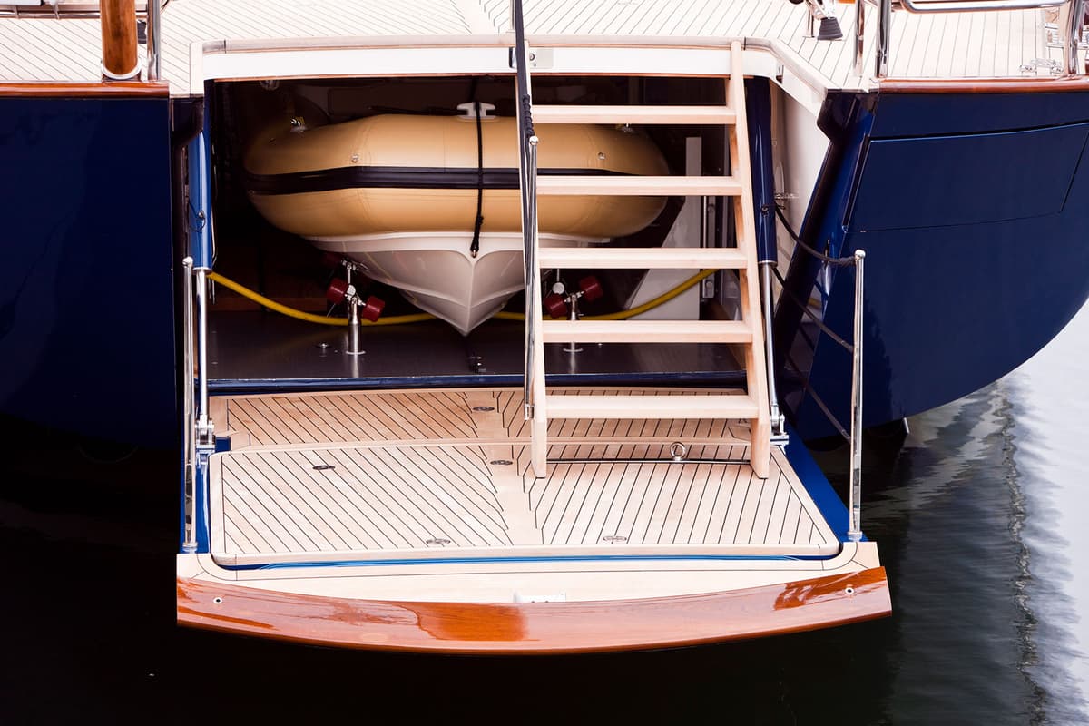 The stern of superyacht Christopher with a wooden staircase leading down to a tender dock, revealing a boat and teak decking.