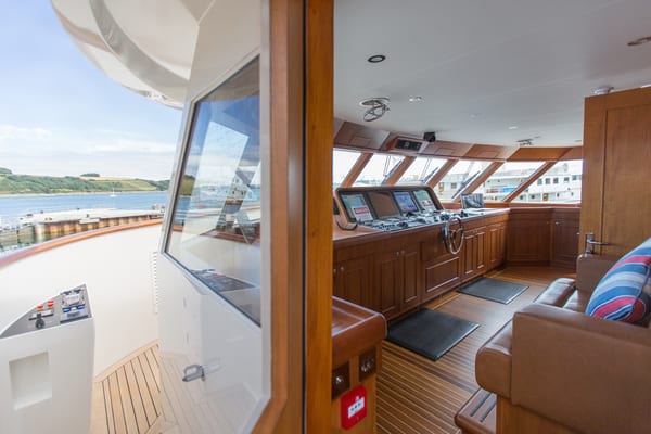 Wheelhouse of superyacht Constance featuring wood paneling, navigation equipment, and access to exterior controls.