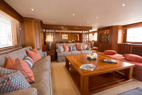 Spacious main salon on superyacht Constance with wood paneling, plush seating, and large windows.