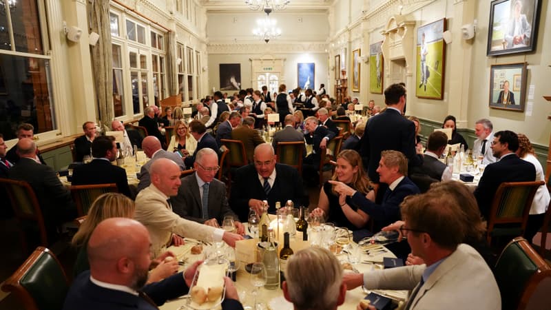 Guests enjoying a formal dinner event in an elegant hall with chandeliers, large windows, and portrait paintings.