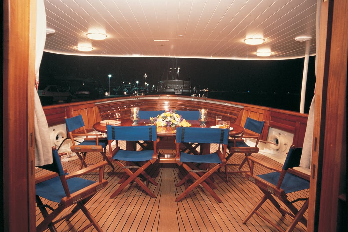 Fair Lady aft deck dining area with wooden seating and blue chairs following her 1996 refit at Pendennis.