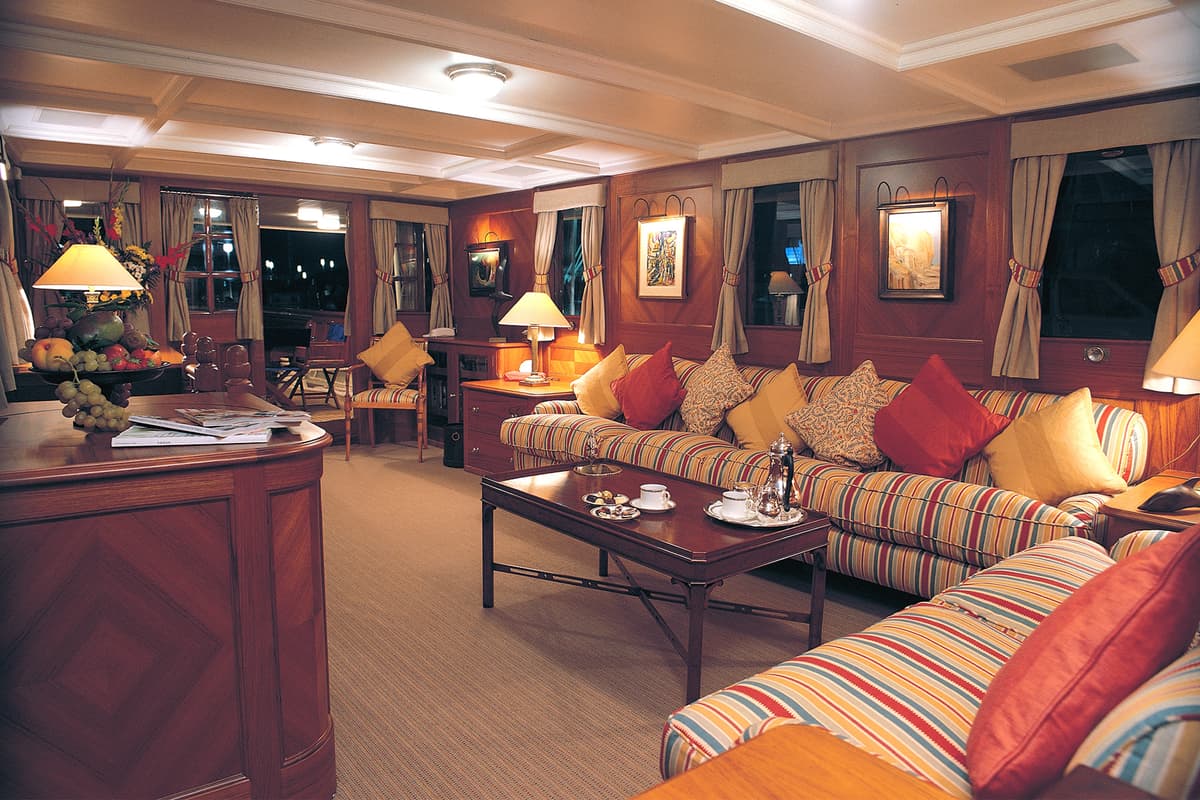Warm and elegant main salon on classic motor yacht Fair Lady featuring striped sofas, wood paneling, and soft lighting.