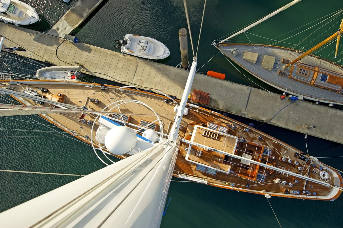 Superyacht Gloria viewed from the masthead while docked at Port Pendennis Marina, showing full teak deck and dock layout.