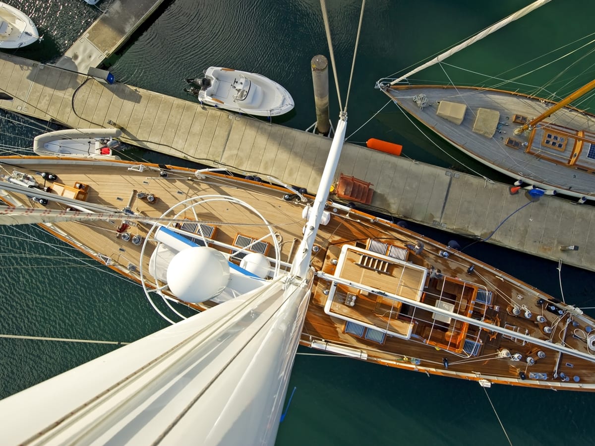 Superyacht Gloria viewed from the masthead while docked at Port Pendennis Marina, showing full teak deck and dock layout.