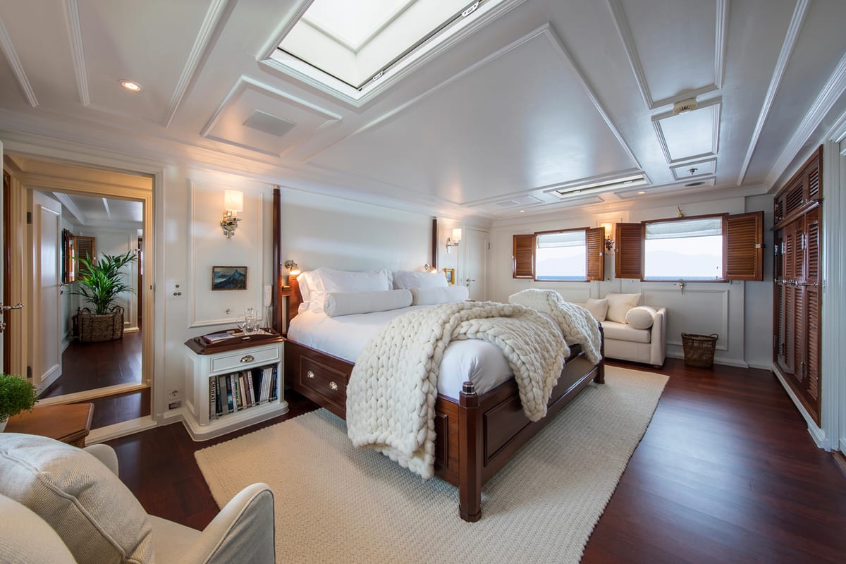 Bright master cabin aboard Haida 1929 featuring a four-poster bed, soft furnishings, and wooden shutters.