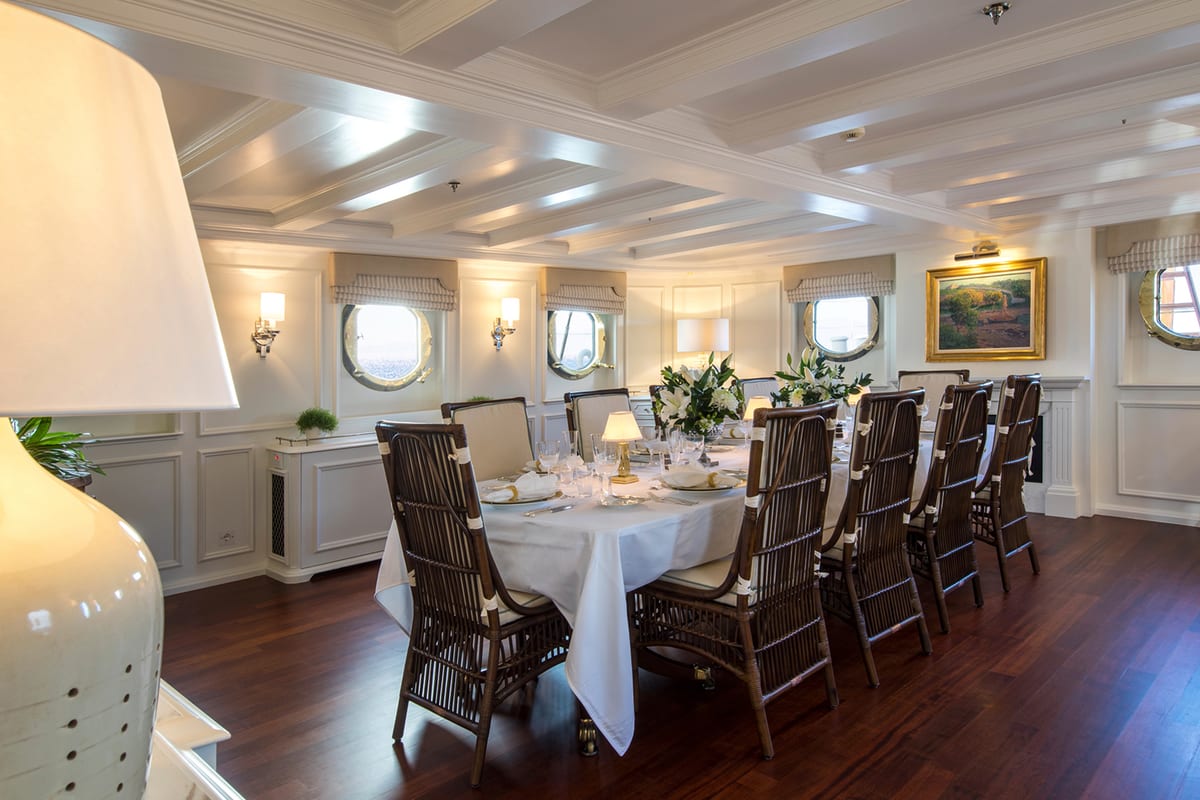 Formal dining room on Haida 1929 with white tablecloth, floral arrangements, and round porthole windows.